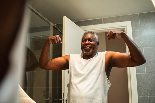 Older man flexing biceps in home bathroom mirror