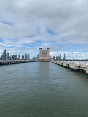 Fototapeta premium Brooklyn Bridge Park pier house control tower rising from waterfront piers amid Manhattan skyline towers under partly cloudy gray skies over East River