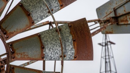 Close-up of a weathered windmill's blades, showing rust and rivets against a cloudy sky