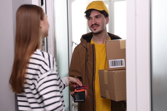 Woman paying for delivery with credit card while receiving parcels from courier indoors