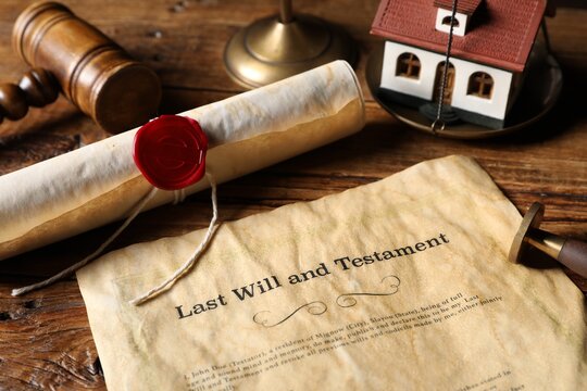 Last Will and Testament, gavel, scroll and house model on wooden table, closeup