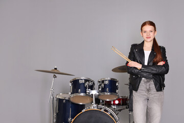 Teenage girl with drumsticks and drums on light grey background. Space for text