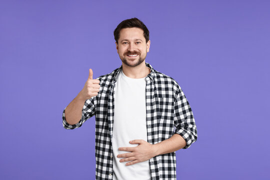 Happy man with healthy stomach showing thumbs up on purple background