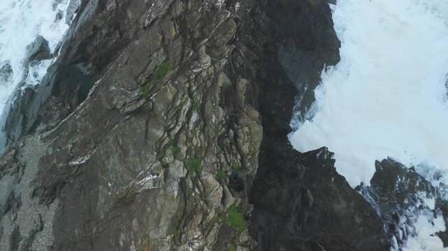 rising up overhead drone shot of woman sitting on cornwall cliffs at newguay making her seem small and tiny