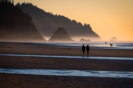 Silhouette of people beach walking during a beautiful sunset along the Oregon coast at Arch Cape. Nothing more enjoyable than walking a wide sandy beach during a glorious sunny evening in Oregon.