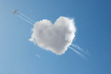 Cute fluffy heart-shaped cloud with plane flying through it as piercing arrow in blue sky