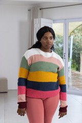 African American woman standing near sliding doors at home in striped sweater and pink leggings