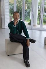 Naklejka premium African American man sitting on beige ottoman in modern living room wearing dark green sweater