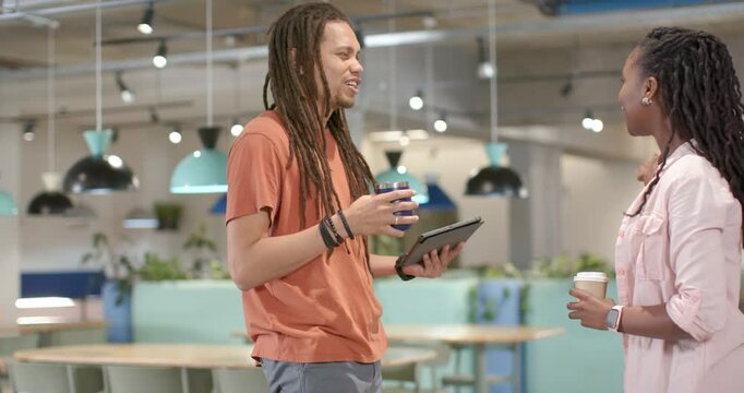 African American coworkers smiling, sparking chat with tablet, mugs in lounge, walking to continue