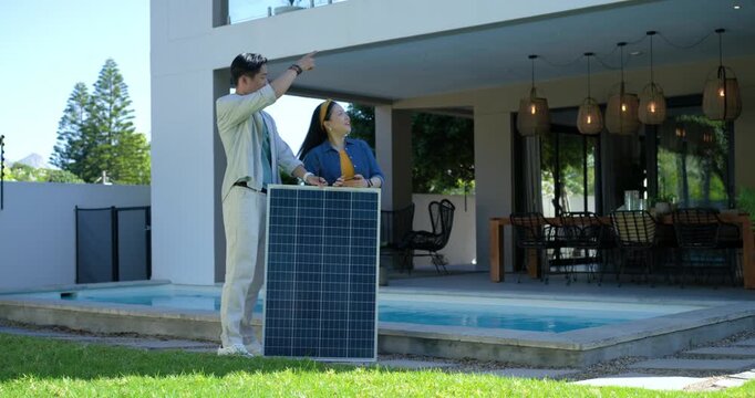 Woman lifting handheld tool, pair are aligning solar panel on lawn by pool for roof mounting