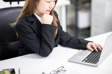 A happy-looking Asian working woman is using a laptop at her desk in a modern office, Business concept