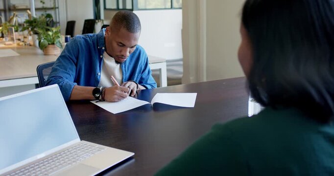 African American team watching man writing and presenting papers with pen laptop after seeing stack