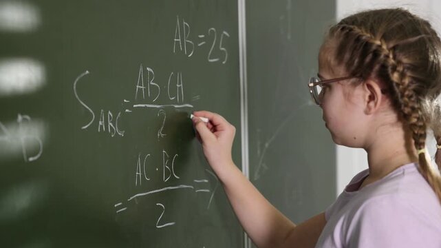 Schoolgirl doing math on chalkboard in classroom
