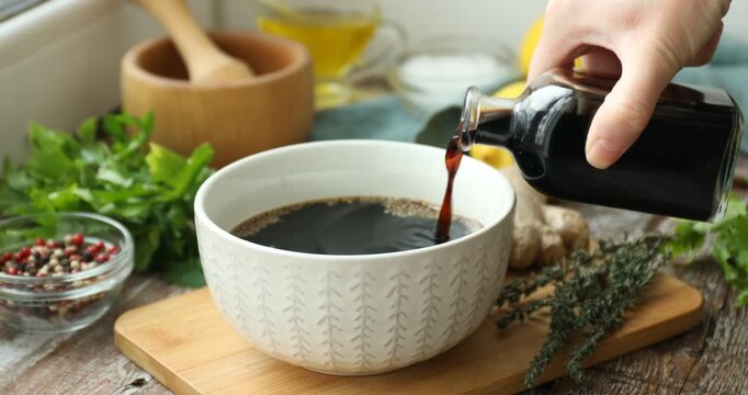 Woman adding soy sauce into bowl with marinade at wooden table, closeup