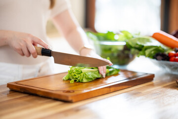 Obraz premium An Asian woman is chopping vegetables to make a salad on the kitchen counter.