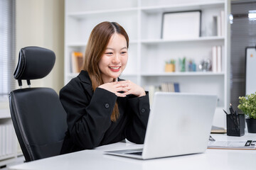 Obraz premium A happy-looking Asian working woman is using a laptop at her desk in a modern office, Business concept