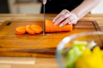 An Asian woman is chopping carrots on a kitchen table to make a salad. The concept of healthy eating and dieting is conveyed.