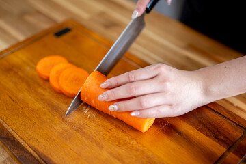 An Asian woman is chopping carrots on a kitchen table to make a salad. The concept of healthy eating and dieting is conveyed.