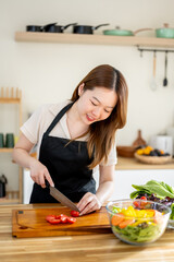 An Asian woman is slicing tomatoes on a kitchen table to make a salad. The imagery relates to healthy eating and dieting.