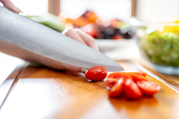 An Asian woman is slicing tomatoes on a kitchen table to make a salad. The imagery relates to healthy eating and dieting.