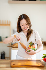 An Asian woman is making a salad in the kitchen. The concept is related to healthy eating and dieting.