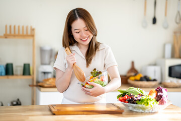 An Asian woman is making a salad in the kitchen. The concept is related to healthy eating and dieting.