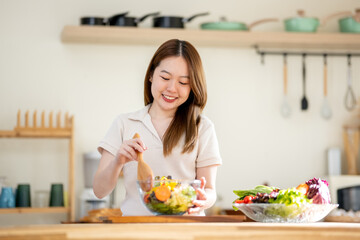 An Asian woman is making a salad in the kitchen. The concept is related to healthy eating and dieting.