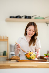 An Asian woman is making a salad in the kitchen. The concept is related to healthy eating and dieting.