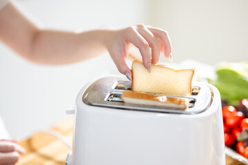 An Asian woman is happily toasting bread for breakfast in the kitchen.