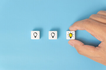 Fototapeta premium Hand picked a dice with the yellow light bulb symbol on blue background. New idea, Innovation and Solution concepts.