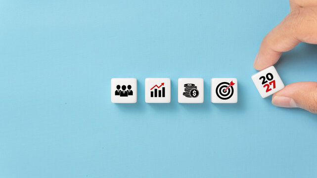 2027 business strategy planning concept with hand placing dice showing icons of team, growth, finance, and target, symbolizing future goals, leadership, development, and success planning
