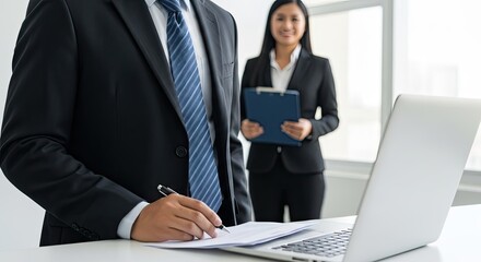 Fototapeta premium Two business professionals in an office setting. One man in a suit and tie, the other in a suit and tie with a clipboard.