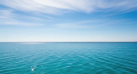 Obraz premium A serene blue ocean with gentle waves and a clear blue sky with a few scattered clouds.