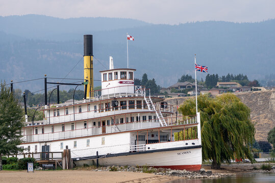 View of the historic sternwheel steamboat Sicamous docked along the lakeshore with mountains in the background.