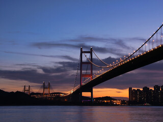 Illuminated Suspension Bridge at Twilight Over Water - Tsing Ma Bridge in Hong Kong