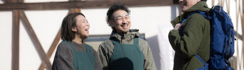 田舎で民宿やペンションを家族経営している接客や受付、チェックインの案内する夫婦と登山者　登山の山小屋などのイメージ　いらっしゃいませ（多摩木材センター協同組合プロパティ許可ずみ）のバナー