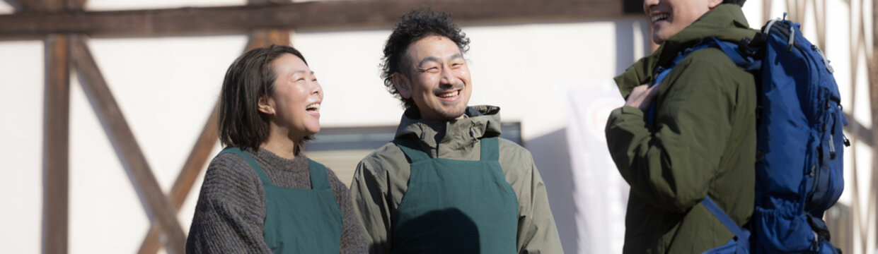 田舎で民宿やペンションを家族経営している接客や受付、チェックインの案内する夫婦と登山者　登山の山小屋などのイメージ　いらっしゃいませ（多摩木材センター協同組合プロパティ許可ずみ）のバナー