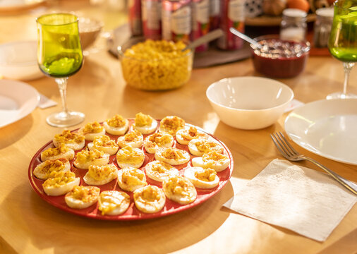 Plate of deviled eggs on wooden table with bowls and drinks in sunlight Thanksgiving holiday