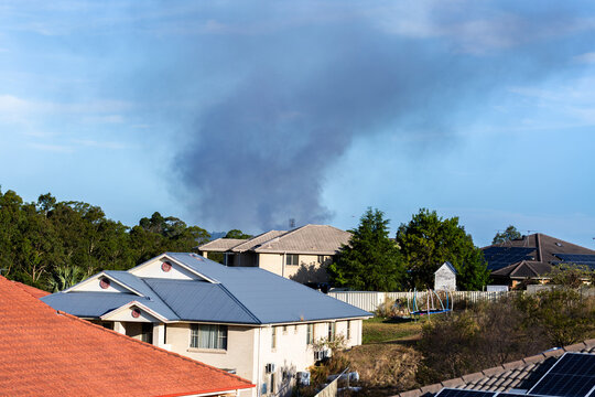 Black smoke billowing into sky behind residential buildings from bushfire near town