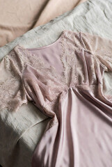 Elegant blush pink women&rsquo;s nightdress featuring delicate lace detailing on soft satin fabric, styled on a cozy bed with neutral bedding.