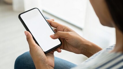 A person holding a smartphone with a blank screen, sitting casually at home, focusing on the device in their hands.