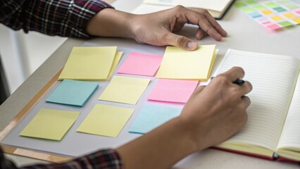 A person organizing colorful sticky notes while writing in a notebook on a clean desk.