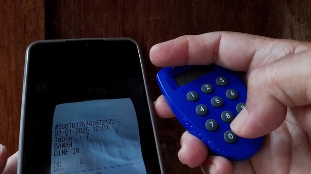 Close up video of hand pressing numeric buttons on a banking security token next to a smartphone screen showing a payment bill, representing digital banking, secure transactions, mobile payments