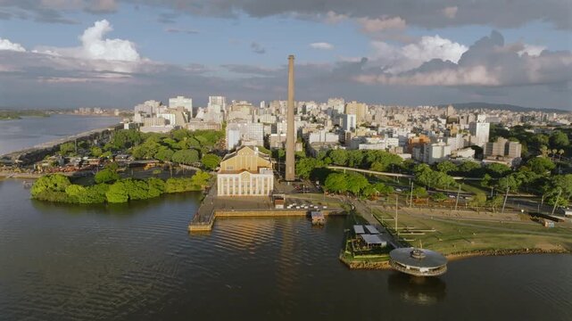 Cinematic aerial drone establishing shot with sideways rising movement revealing Porto Alegre city skyline, Usina do Gasometer and Guaiba Lake during golden hour sunset in Brazil. 4K 60fps 10-bit