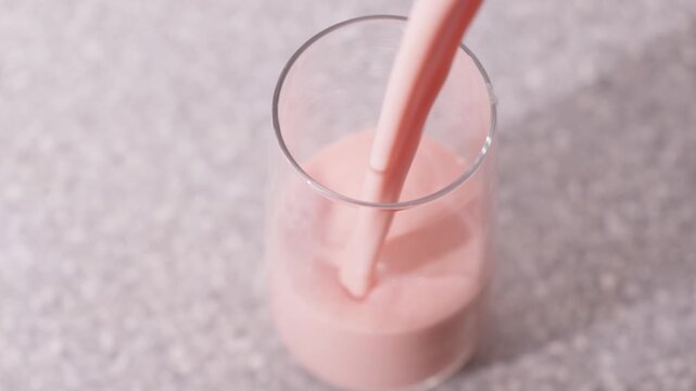 Simple, pouring a blended healthy fruit pink coloured smoothie into a glass drinking tumbler on a bench. Clip 2