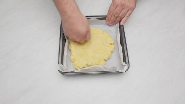 Hands spreading cake batter evenly in a baking tray lined with parchment paper.