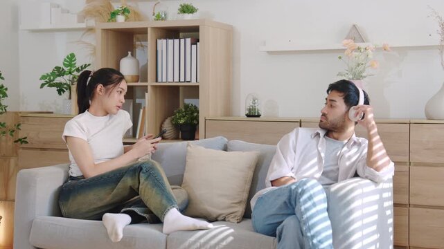 Young couple sitting separately on couch at home while avoiding eye contact, representing relationship conflict, misunderstanding, emotional distance, and silent treatment in modern lifestyle.
