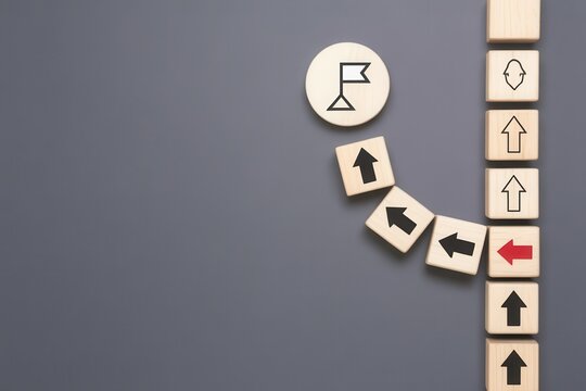 Business strategy concept with wooden blocks showing path deviation towards a goal flag on dark background