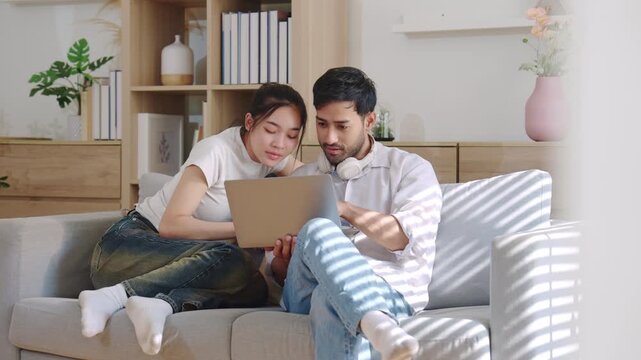 Happy couple sitting on couch and looking at laptop together in cozy living room, representing teamwork, online activity, modern home lifestyle, and digital communication.