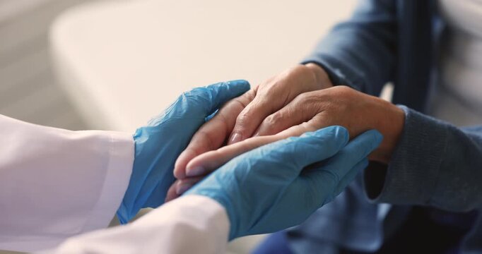 Close up female doctor hands in rubber gloves gently holds of woman patient arms, offering psychological, emotional support during medical consultation at hospital. Trust, empathy, health care service